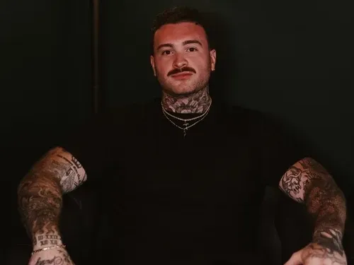 Portrait of Zach seated with his tattooed arms visible