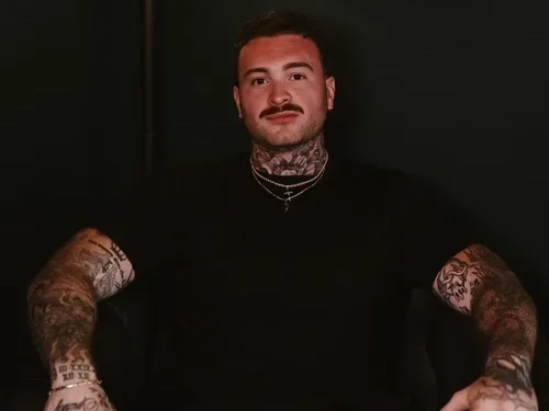 Portrait of Zach seated with his tattooed arms visible